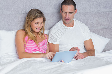 有吸引力的年轻夫妇在床上一起使用平板板电脑图片