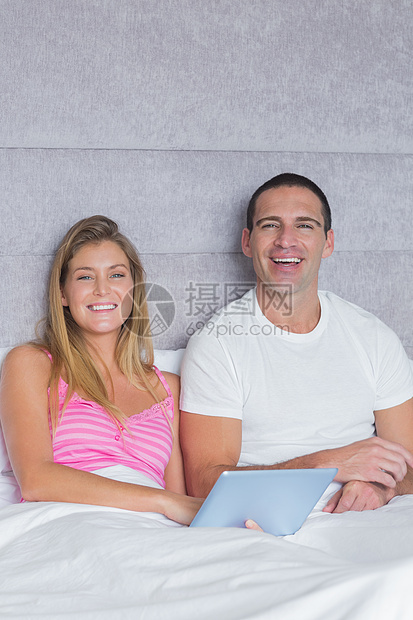 在床上用平板电脑一起微笑的年轻情侣图片