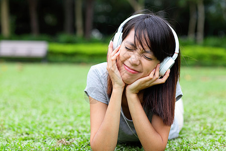 亚洲女人听草地上的歌说谎歌曲耳机女士耳朵音乐女孩植物青少年女性图片