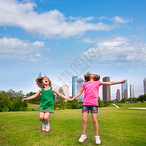 两个女孩在城市天际上 握着手 快乐地跳过两个朋友景观姐妹家庭金发旅行草地商业建筑学跳跃建筑物图片
