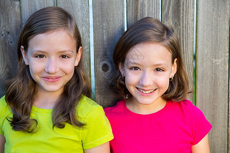 幸福的姐妹姊妹在木林后院篱笆上微笑快乐家庭木头冒充倾斜双胞胎乐趣金发孩子们孩子图片