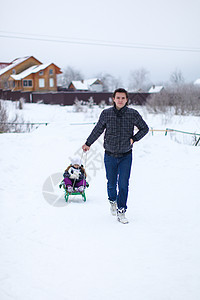 小爸爸在雪地外的雪橇上 卷起他可爱的小女儿男人父母乐趣家庭微笑成人快乐父亲季节闲暇图片