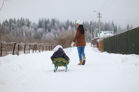 年轻母亲在冬天的雪橇上 卷起她可爱的小女儿帽子晴天闲暇家庭童年女孩幸福母性父母孩子图片