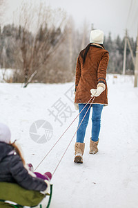 年轻母亲的后视镜在冬日雪橇上滚动着她可爱的小女儿孩子快乐帽子童年娱乐家庭闲暇微笑青年喜悦图片