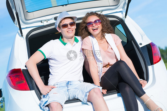 年轻夫妇坐在露天后备箱帽子微笑女性快乐成人夫妻车轮运输男性旅行图片
