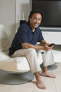坐在现代客厅里 一个快乐的亚洲男人的肖像 在家中大型电视屏幕前 有遥控器的遥控室图片