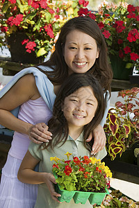 母亲和女儿在植物苗圃肖像中拿着年轻鲜花图片