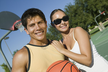 一对微笑的年轻夫妇在法庭上打篮球的肖像图片