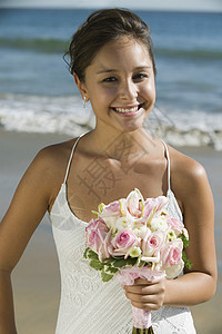 在海滩上站立着花束的幸福新娘的肖像图片