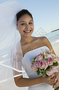 快乐的年轻新娘在海滩上拿着花束的肖像图片