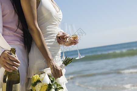 新婚夫妇的中产区 在海滩上加香槟瓶和长笛团结新郎婚礼庆典天空裙子夫妻男士仪式传统图片