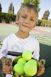 在网球场的男孩 拿着Trophy 充满网球球肖像图片