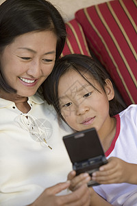 母亲和女儿在沙发上玩手持视频游戏图片