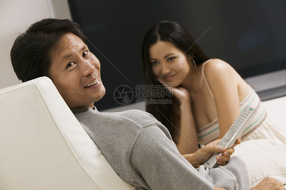 一对夫妇坐在大片平板屏幕电视肖像机上图片