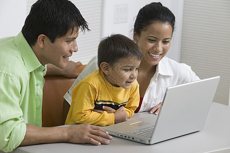 快乐的一对夫妇和儿子 在书桌上用笔记本电脑图片