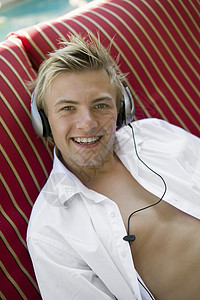 坐在甲板椅上的年轻人 通过游泳池听音乐 在耳机肖像图片