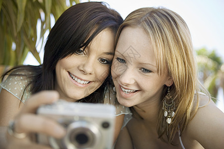 两名年轻妇女在后院前视镜中观看数码相机照片 她们图片
