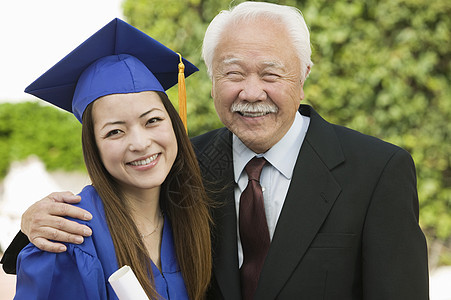 快乐的女毕业生和祖父在户外站立的肖像图片