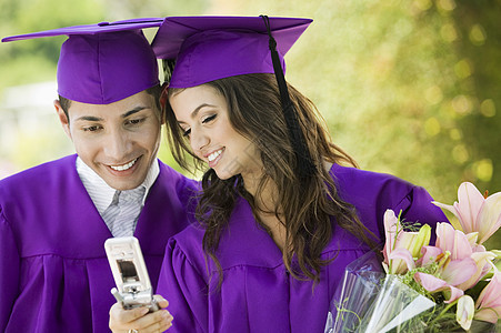 快乐的男女毕业生在户外看手机时观看电话图片