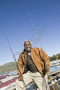 速度与激情0快乐的非洲裔美国人男子与渔棍站在一起 船背着背景 他们站在钓鱼杆上背景