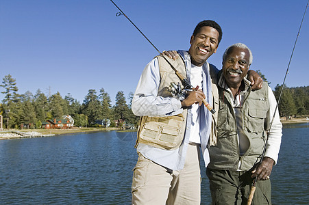 幸福的老年男子和成年儿子在湖边持有渔棍的肖像图片