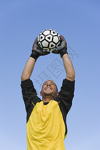 青年守门员在蓝天和蓝色天空上 追足球球的低角度视角图片