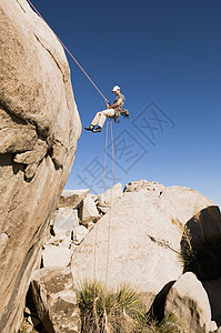 一个年轻人从悬崖上 与清蓝天空相交的低角度视角图片