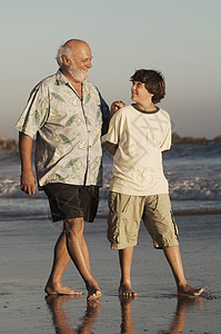 整个快乐的祖父和孙子 在黄昏时在海滩上散步图片