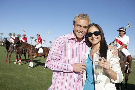 一对夫妇的肖像 拿着香槟杯 与马球运动员在背景图片