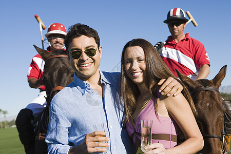 快乐情侣的肖像 站在和两个马球运动员 在背景图片