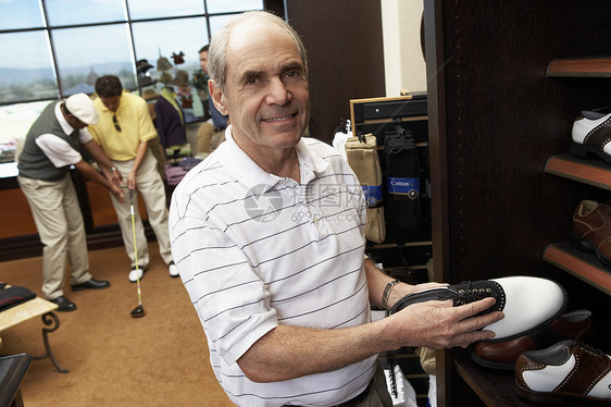 快乐的老年男子与背景人一起挑选在店里储存的鞋子的肖像图片