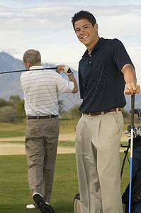一个快乐的年轻男性高尔夫球手 和男人在背景中玩耍的肖像图片