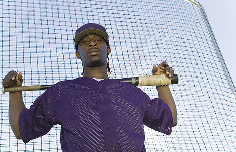 一个充满自信的棒球运动员在练习时拿着球棒与网对打的肖像图片