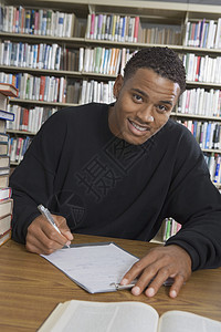 一名非裔美国男性学生在大学图书馆作笔记时的肖像图片