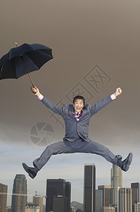 满身狂喜的商务人士 用雨伞在半空中跳跃图片