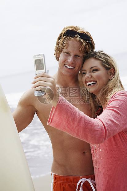 快乐的一对年轻夫妇与冲浪板 在海滩上通过手机进行自画像图片