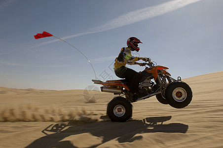 一个四轮骑自行车的车手在沙漠中 与天空对立的侧边景色图片