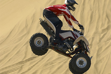 半空中的四轮自行车骑手在沙漠沙滩上的侧面视图图片