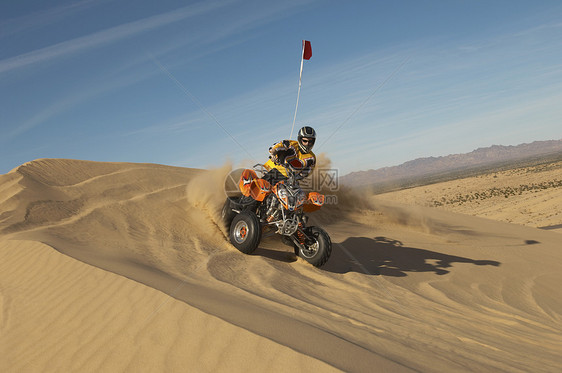 一个男子在阳光明媚的日子里 在沙漠骑四轮自行车的低角度视角图片