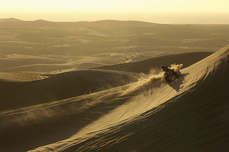 日落时在沙漠骑四轮自行车的男子图片