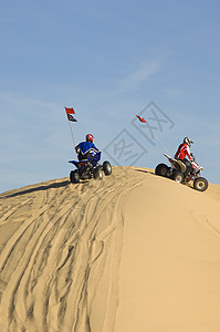 两个年轻人骑着四轮自行车 在沙漠的沙丘上图片