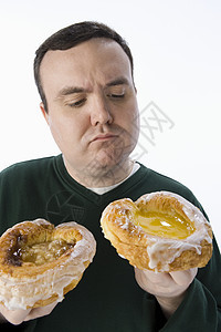 中年男子在两个甜甜圈之间做出选择 两只甜甜圈被白种背景隔绝图片