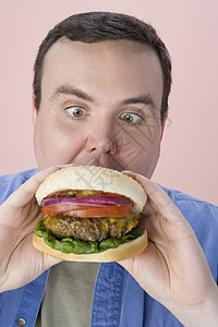 中年男子在粉红背景上吃汉堡包图片