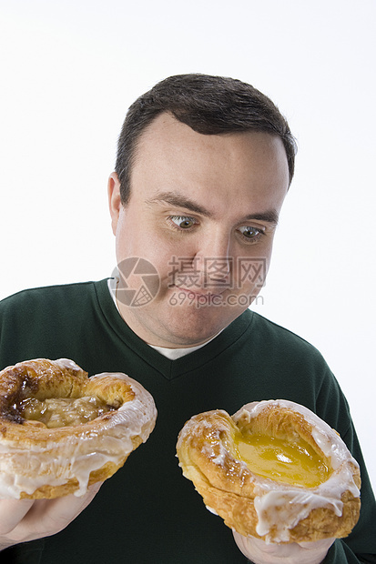 中年男子在两个美味甜甜圈之间做出抉择 两者隔绝于白种背景图片