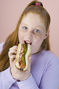 少女吃热狗的肖像与粉红背景隔绝图片