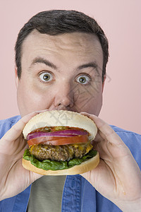 中年男子在粉红背景上吃汉堡的肖像图片