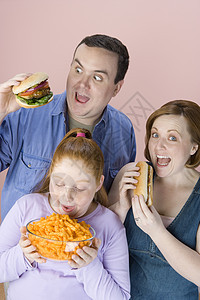 肥胖家庭在吃垃圾食品时 与粉红背景隔绝图片