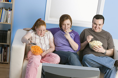 超重家庭在沙发上看电视贪婪客厅食物微笑娱乐三个人土豆家长小吃饮食图片