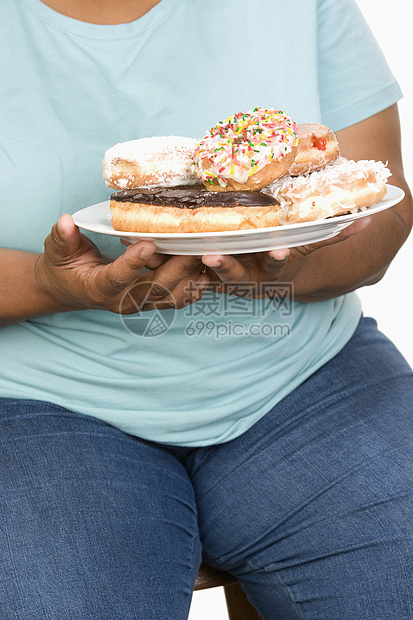 一位肥胖妇女与甜甜圈餐盘一起坐在白背景上被孤立的胖女人的中产体图片
