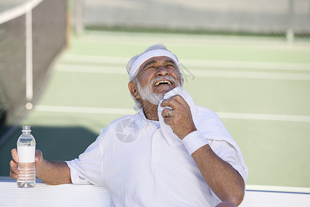 快乐的老年男性网球运动员 用水瓶擦汗用餐巾纸图片